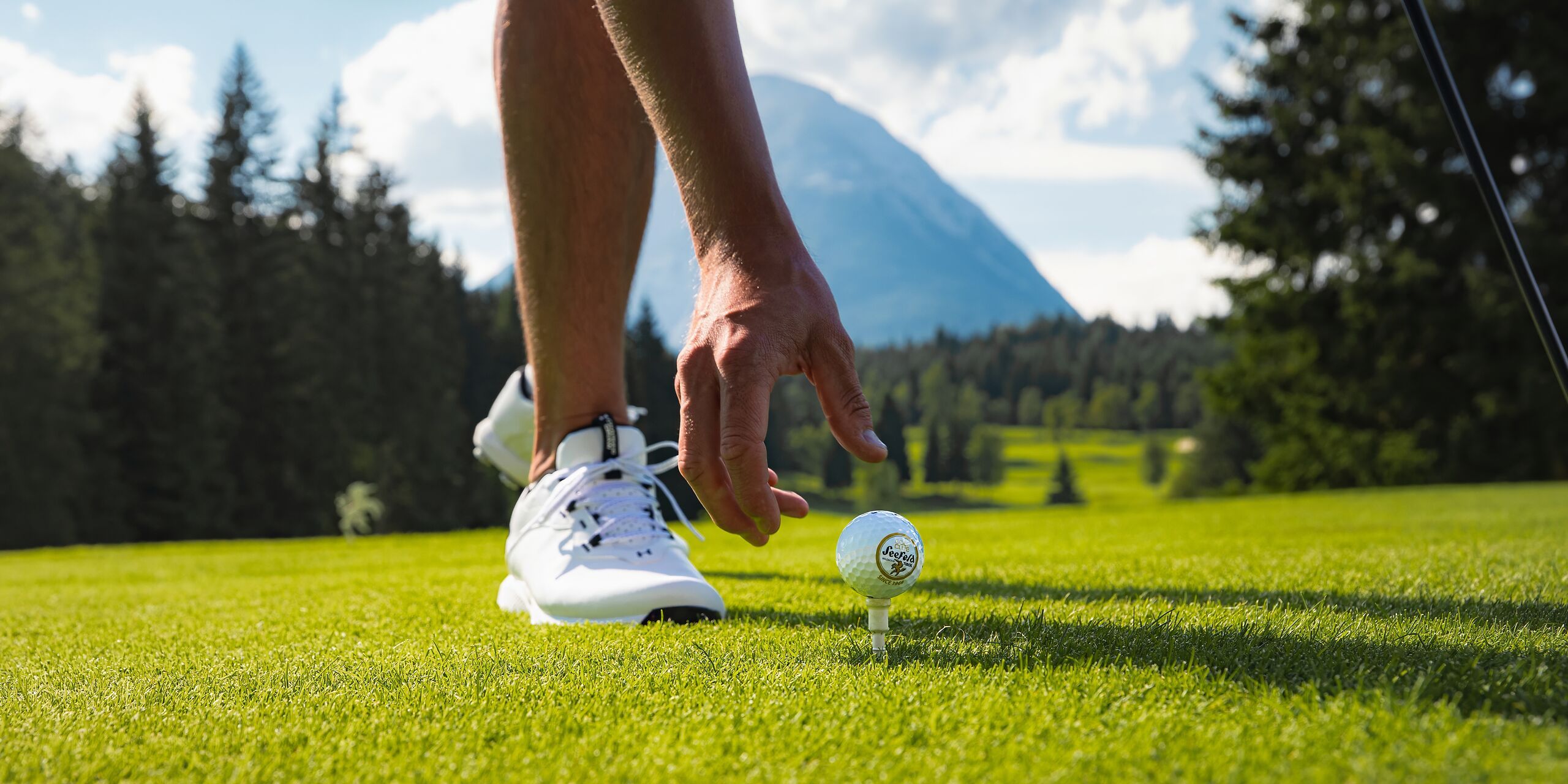 © Region Seefeld | Golfen im GC Wildmoos im Sommer_Nahaufnahme Golfer legt Ball auf Abschlagspunkt