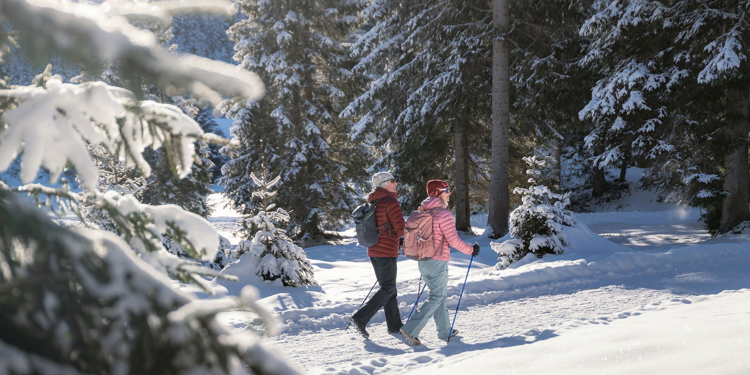 Winterwandern in der Region Seefeld_Mann und Frau laufen wandern im Wildmoos_Aufnahme von hinten mit verschneiten Ästen im Vordergrund
